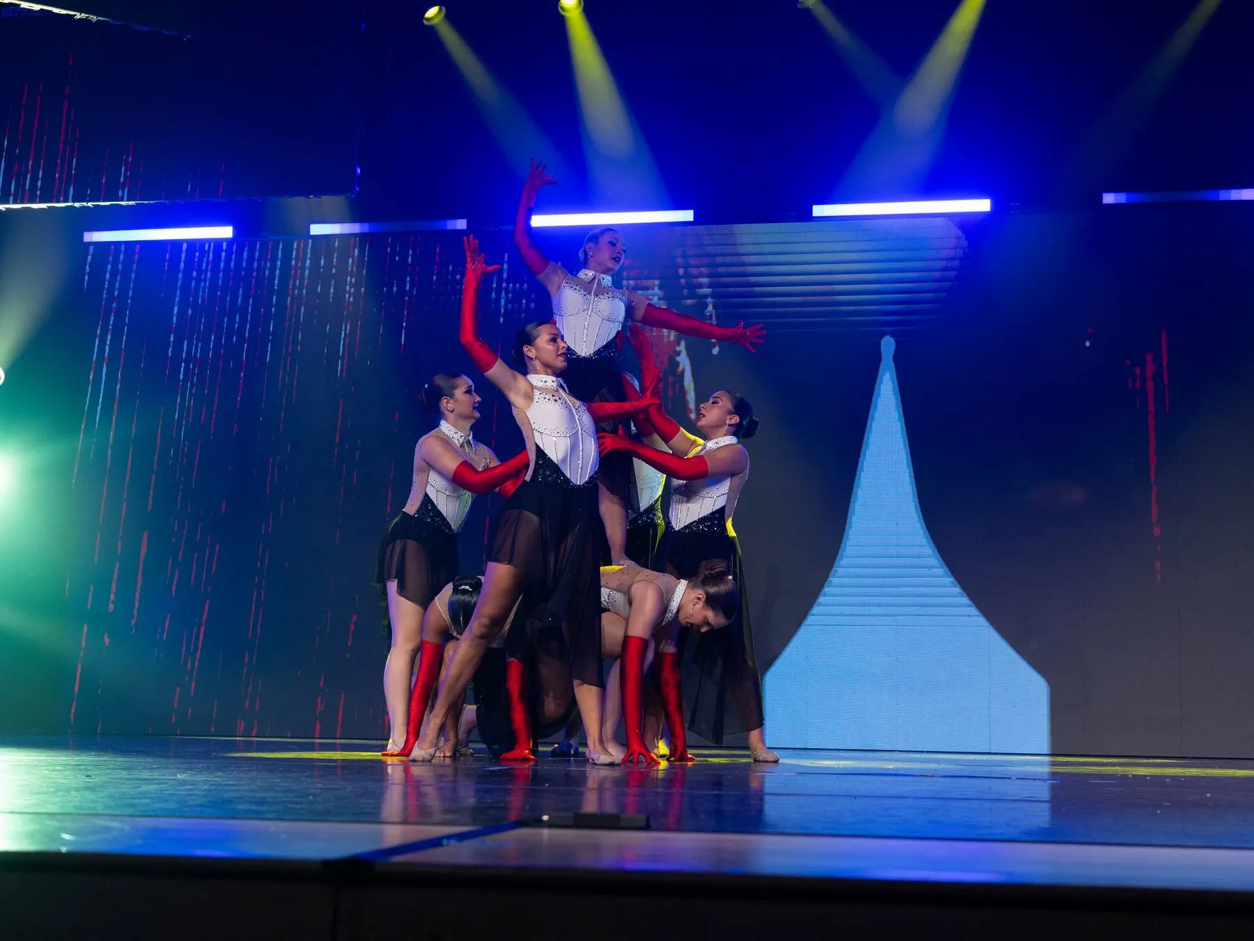 A partnered cluster in red opera gloves, one dancer lifted at the top of the shape