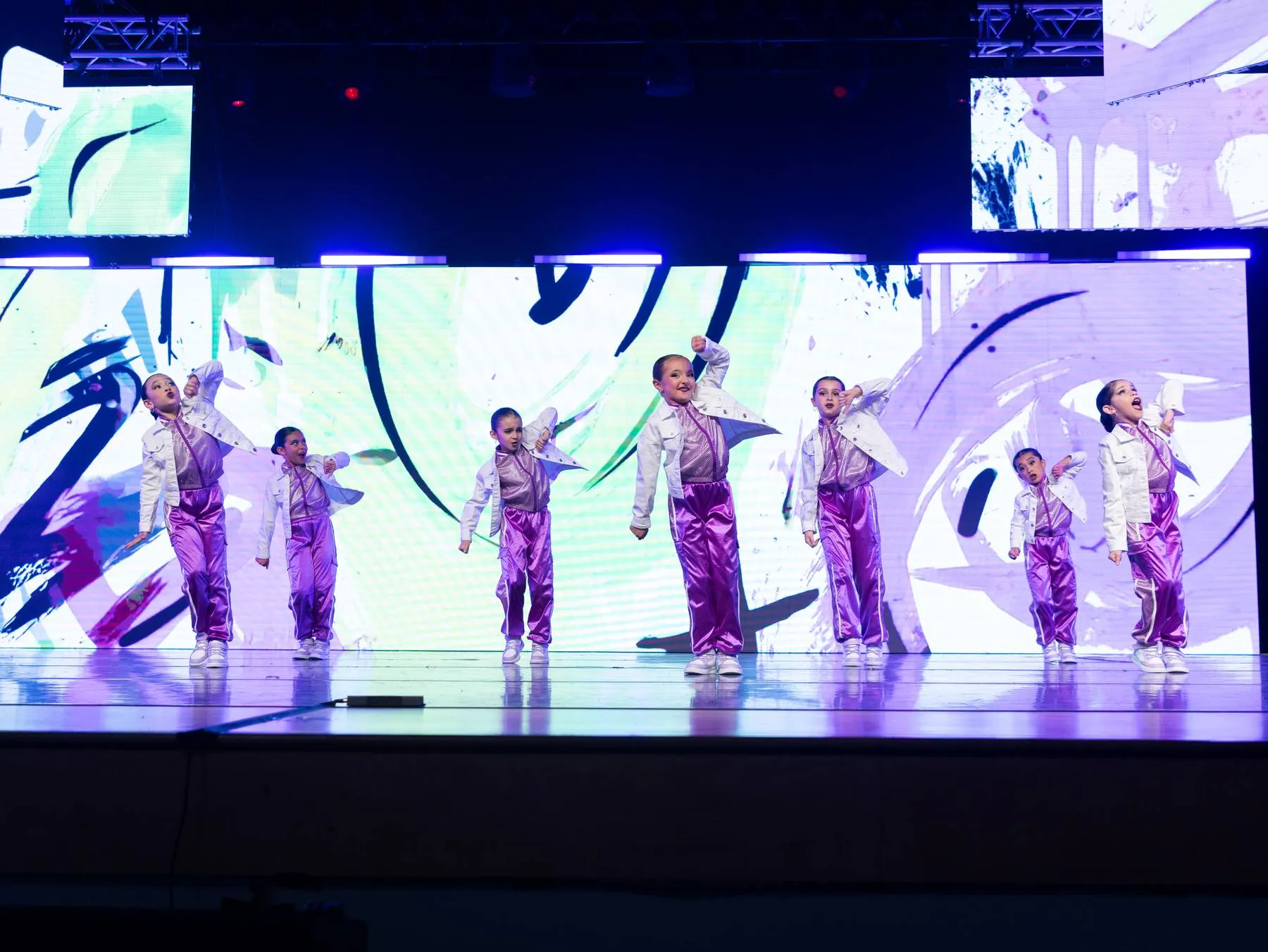 The youngest hip hop group in violet, fists up, graffiti washing the LED wall